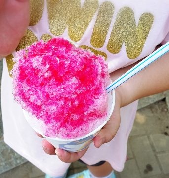 A young girl holds a serving of fluffy Hawaiian shave ice to the camera.