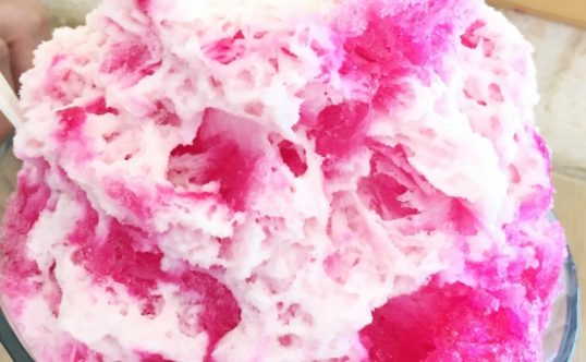 A close up of a large and fluffy serving of pink Hawaiian shave ice.